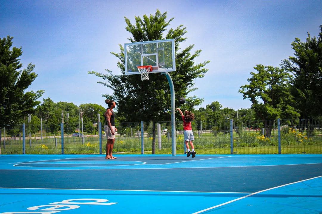 Adult and child playing basketball on a bright blue outdoor court